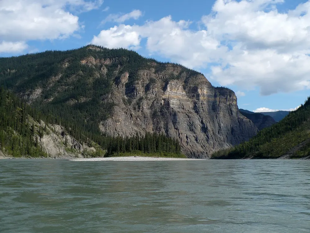 Third Canyon am South Nahanni River: breiter Fluss vor steilen, bewaldeten Kalksteinwänden unter Wolken