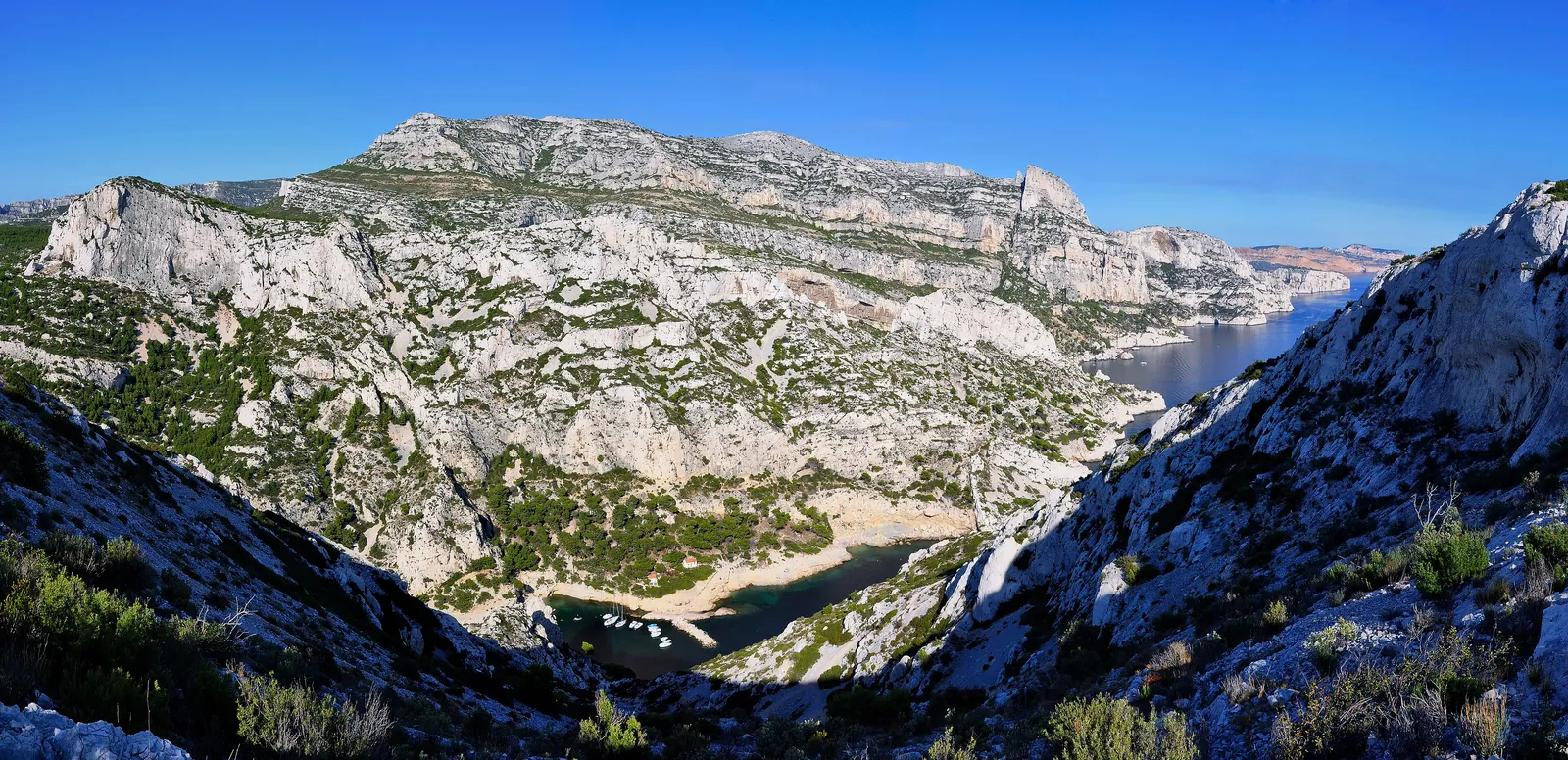 Die Calanque de Morgiou im Nationalpark Calanques von den Klippen aus: Kalkhänge mit Kiefern, unten die Bucht mit kleinem Hafen