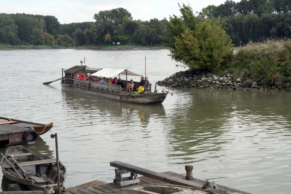 Eine Tschaike mit Dach auf der Donau beim Uferhaus Orth im Nationalpark Donau-Auen, vorn Holzboote am Steg