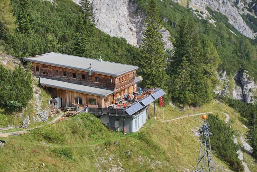 Das Buchsteinhaus im Nationalpark Gesäuse, ein Holzbau mit Terrasse am grünen Steilhang vor hellen Felswänden