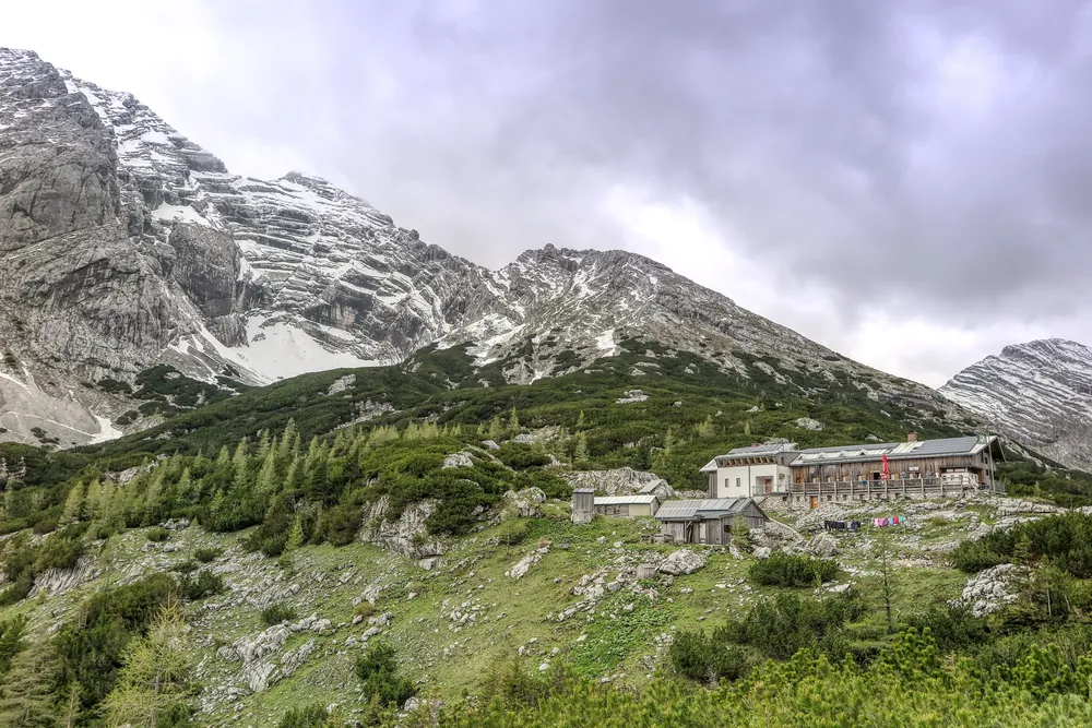 Die Heßhütte an der Grenze des Nationalparks Gesäuse auf einem Latschenhang unter schneefleckigen Kalkgipfeln