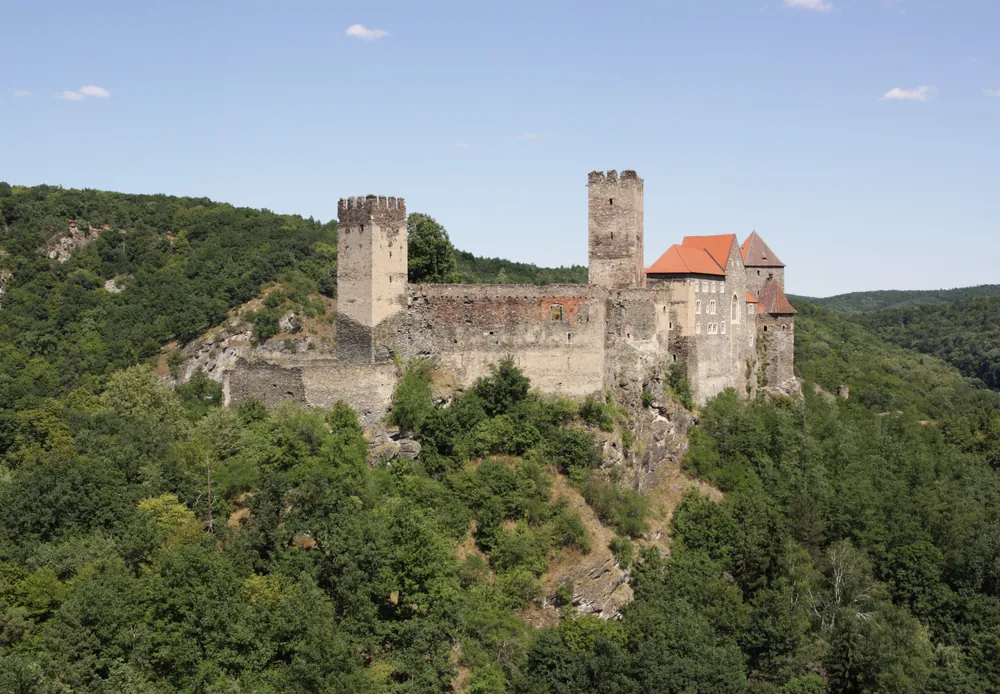 Die Burg Hardegg mit zwei Türmen und roten Dächern über bewaldeten Hängen im Nationalpark Thayatal, gesehen vom Reginafelsen