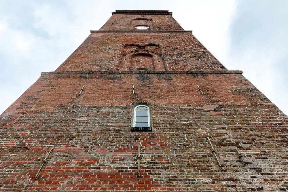Alter Leuchtturm auf Borkum: hoher Backsteinturm in steiler Untersicht vor hellem, bewölktem Himmel
