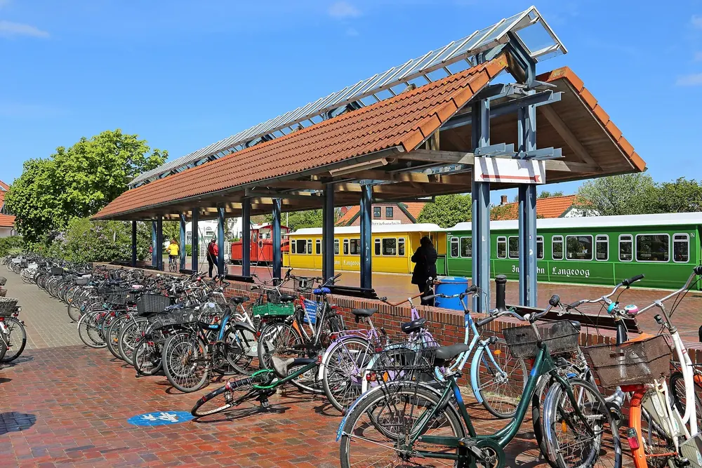 Inselbahnhof Langeoog: überdachter Bahnsteig mit bunter Inselbahn, davor viele abgestellte Fahrräder