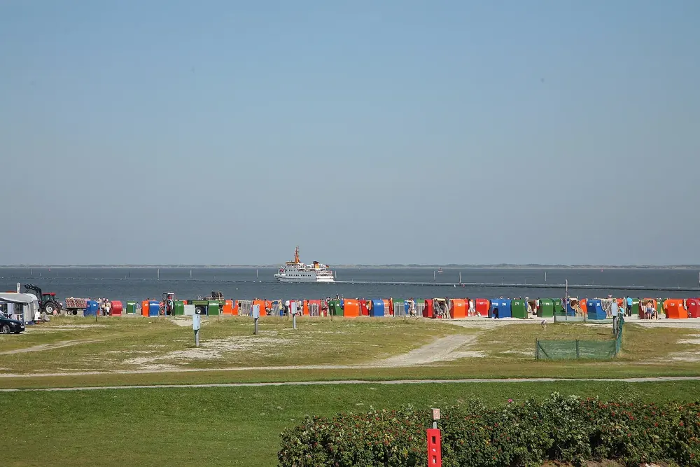Badestrand von Neßmersiel mit bunten Strandkörben, dahinter auf dem Wasser die Fähre nach Baltrum