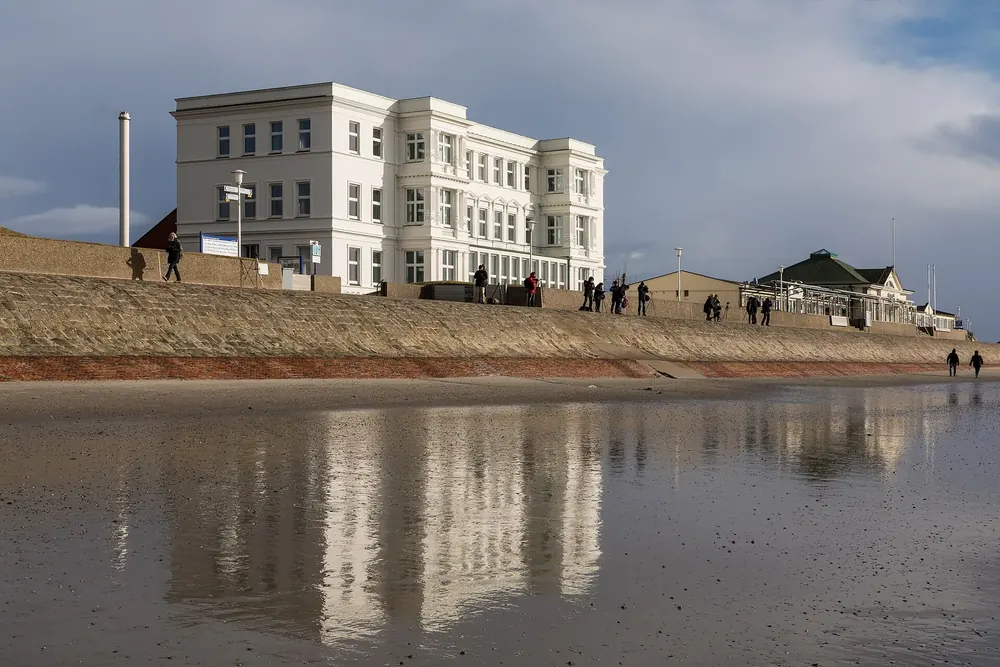 Weststrand von Norderney: das weiße ehemalige Haus Hanebuth spiegelt sich im nassen Sand vor der Strandpromenade