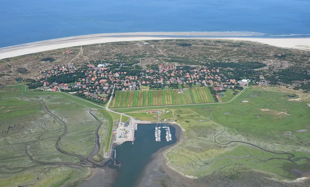 Luftaufnahme von Spiekeroog aus Süden: Inseldorf mit Hafen, Salzwiesen und Prielen, dahinter Dünen und Strand
