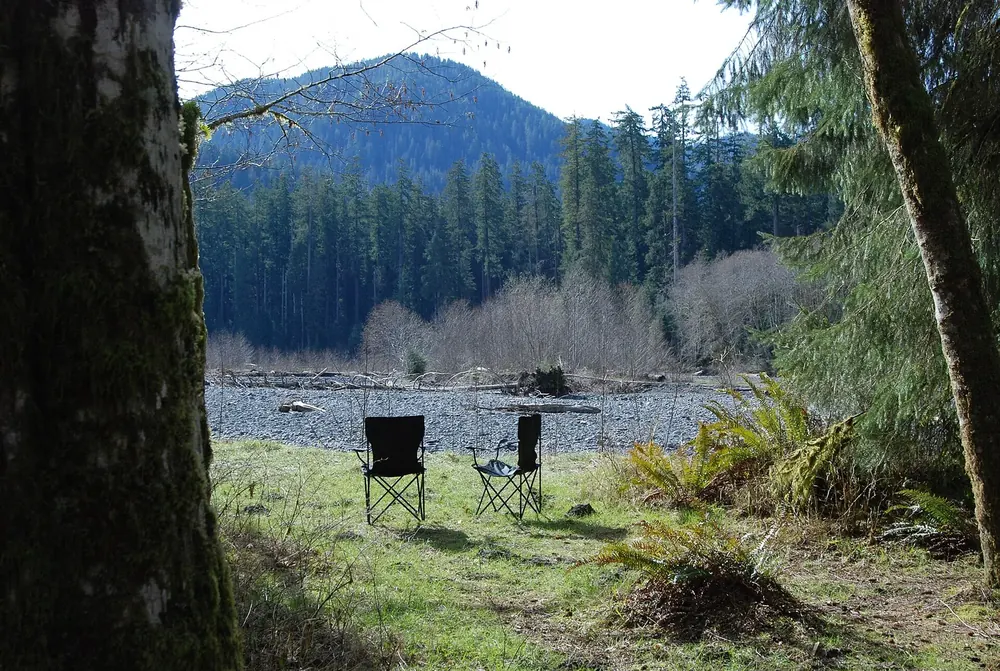 Zwei Campingstühle auf einer Wiese im Hoh Campground, dahinter das Kiesbett des Hoh River und bewaldete Berge
