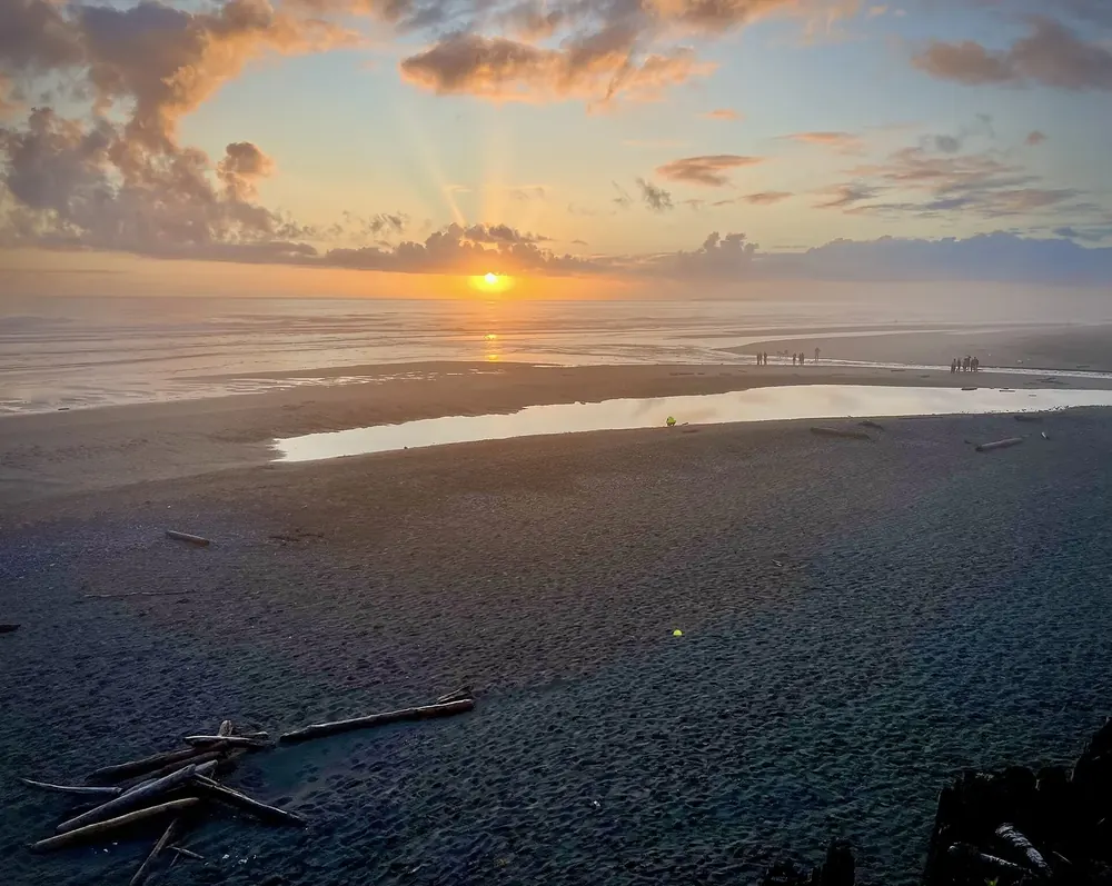 Sonnenuntergang am Strand der Kalaloch Lodge: Sonnenstrahlen über dem Pazifik, im Vordergrund nasser Sand und Treibholz
