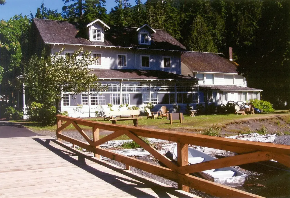 Lake Crescent Lodge vom Bootssteg aus: weißes Holzhaus mit verglaster Veranda, davor Holzgeländer und Rasen