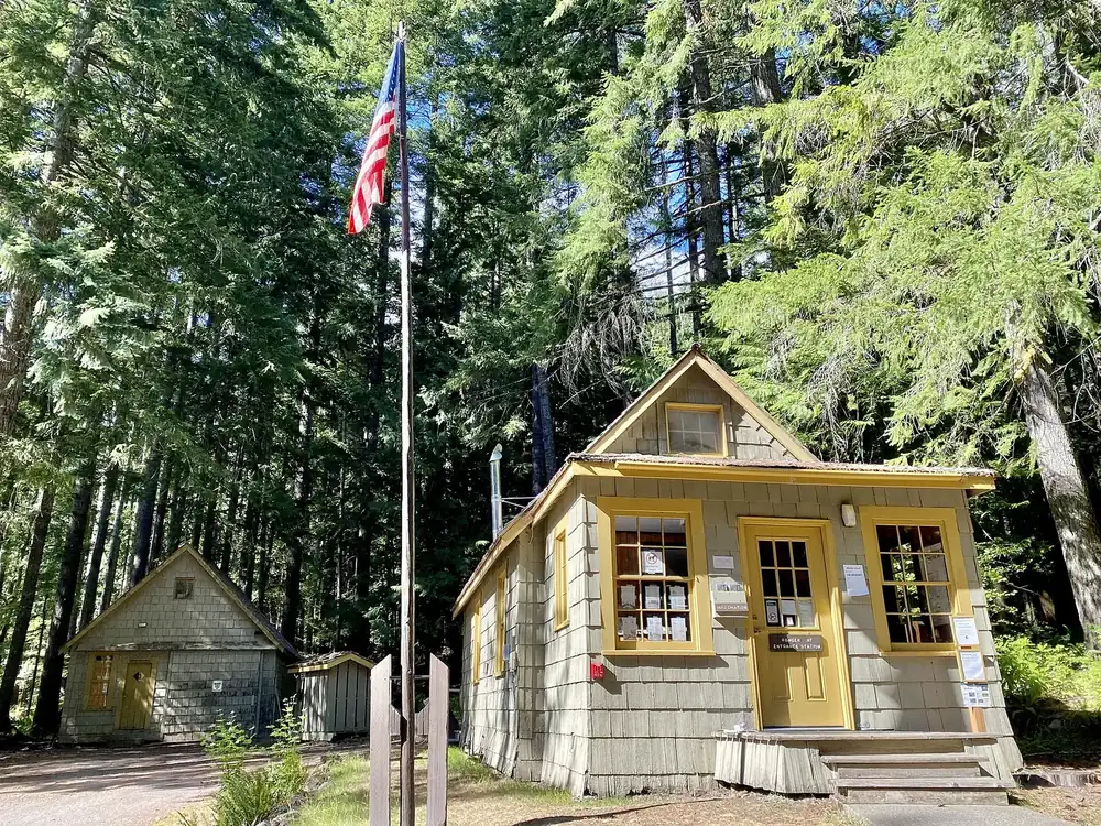 Staircase Ranger Station: kleines Holzhaus mit gelben Fenstern und Fahnenmast unter hohen Nadelbäumen