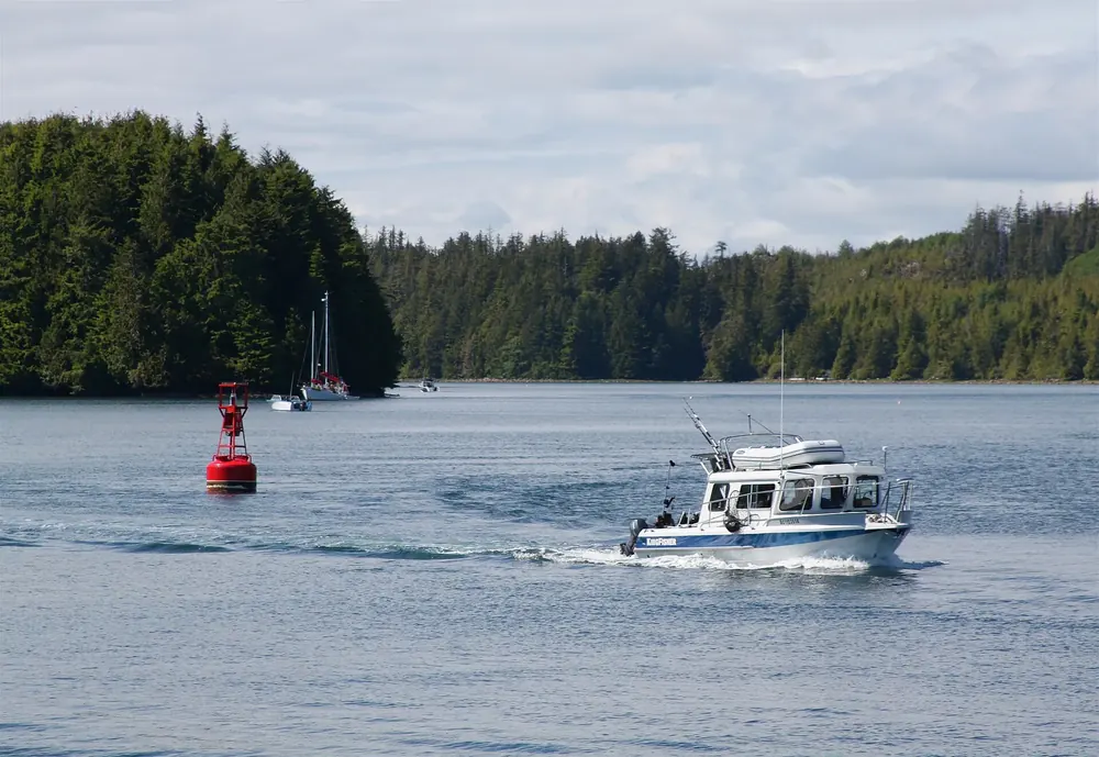 Fischerboot im Meeresarm von Ucluelet, dahinter bewaldete Hänge und ankernde Segelboote