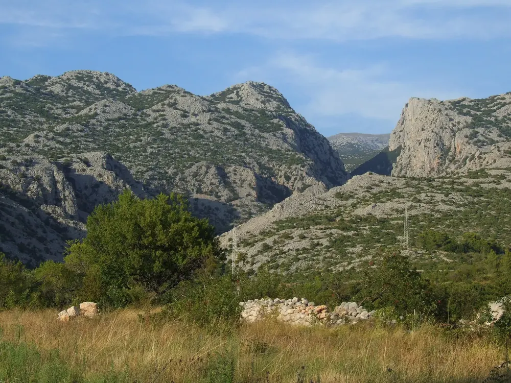 Eingang zur Mala Paklenica: karge Kalkberge mit tief eingeschnittener Schlucht, davor Wiese und Büsche