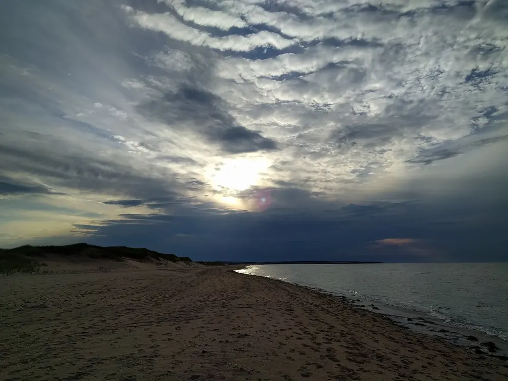 Cavendish Beach in der Abenddämmerung: langer roter Sandstrand mit Dünen unter dramatischem Wolkenhimmel