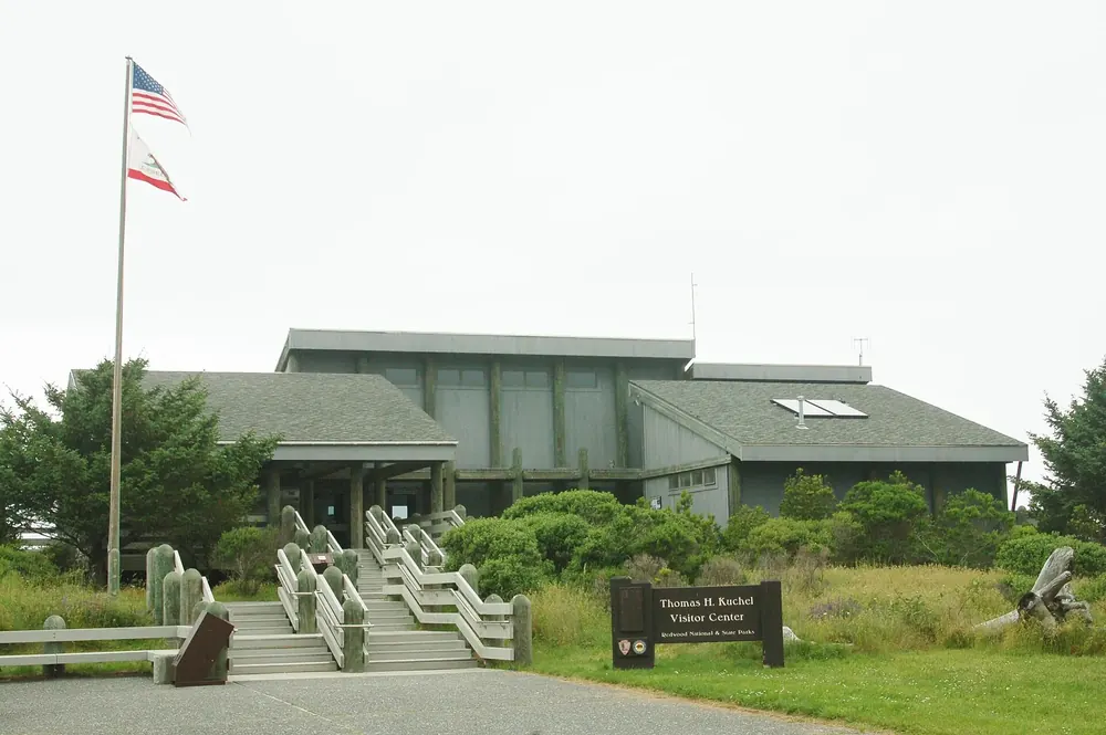 Thomas H. Kuchel Visitor Center: flaches Holzgebäude mit Treppenaufgang, Fahnenmast und Küstenvegetation