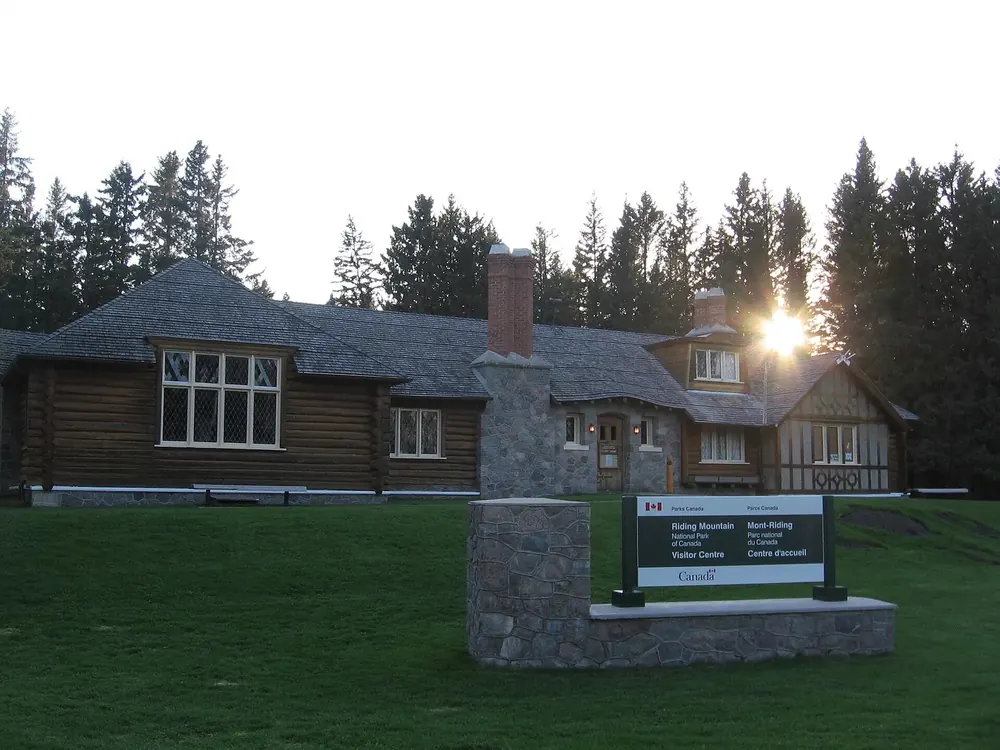 Besucherzentrum des Riding-Mountain-Nationalparks in Wasagaming: Blockhaus mit Steinkamin, davor Rasen und Schild