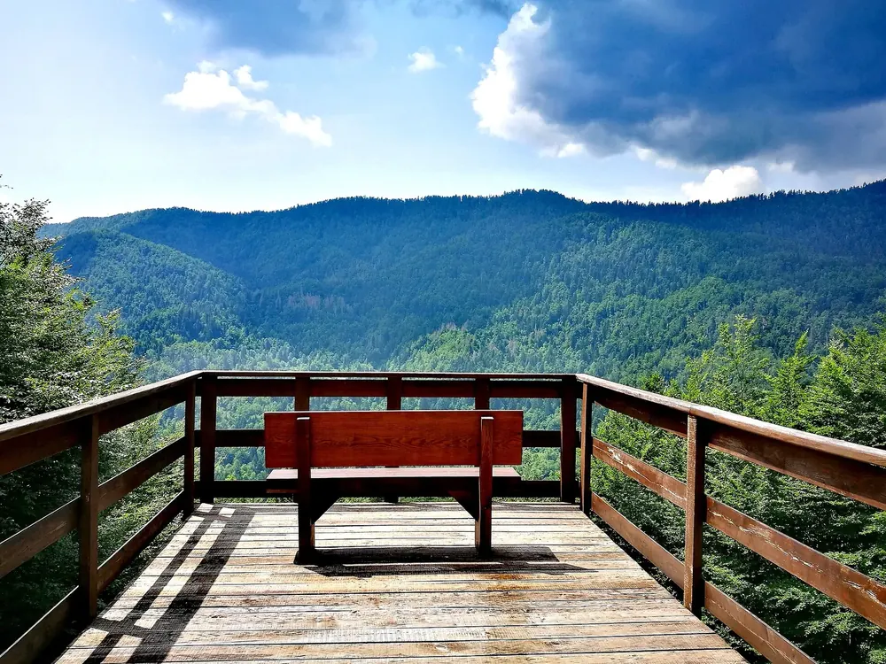 Aussichtsplattform Razloge im Nationalpark Risnjak: Holzbank vor dicht bewaldeten Bergen unter Wolken