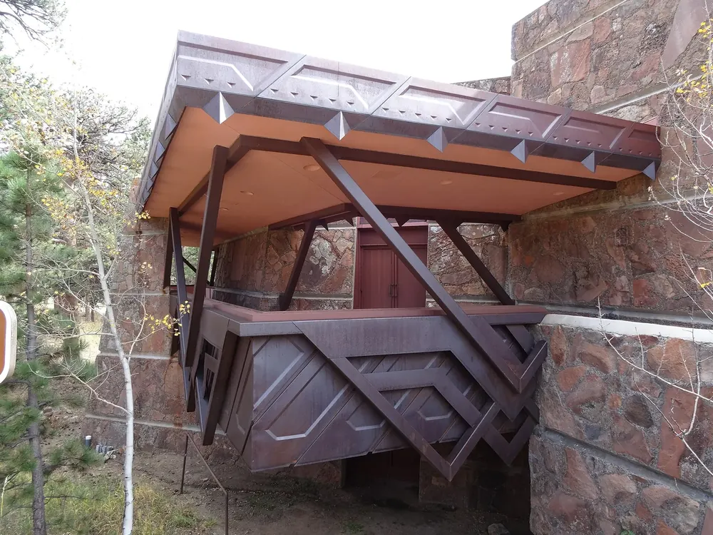 Beaver Meadows Visitor Center: auskragender Balkon aus rostrotem Stahl an einer Natursteinfassade, daneben Laubbäume