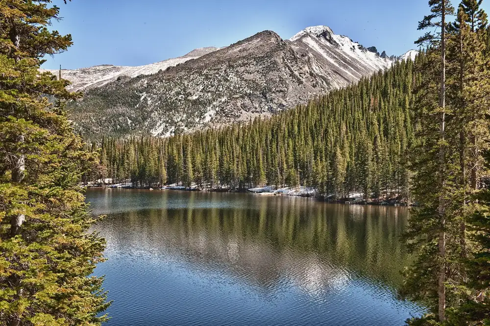 Mills Lake in der Glacier Gorge: stiller Bergsee mit Spiegelungen vor bewaldeten Hängen und felsigen Gipfeln
