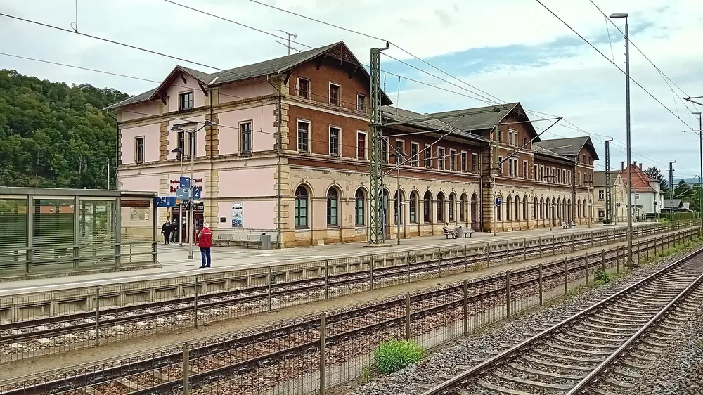 Nationalparkbahnhof Bad Schandau: langes historisches Empfangsgebäude hinter Bahnsteigen und Gleisen unter Oberleitungen
