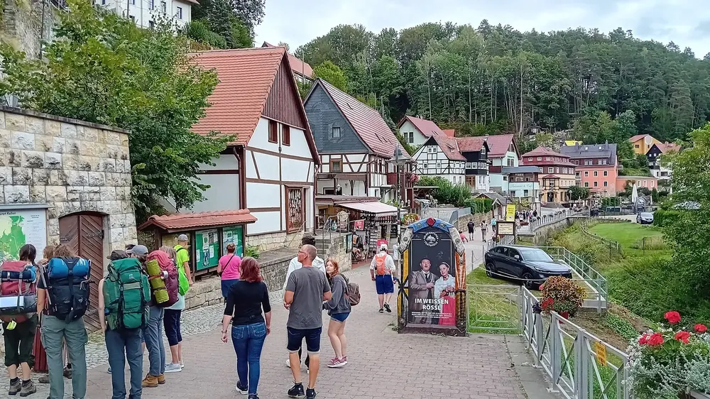 Ortsmitte von Kurort Rathen: Gasse mit Fachwerkhäusern, Wanderern und Blick auf die Felsen der Sächsischen Schweiz