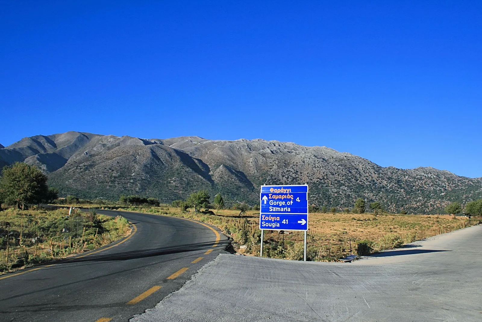 Straße über die Hochebene von Omalos mit Wegweiser zur Samaria-Schlucht, dahinter die Weißen Berge