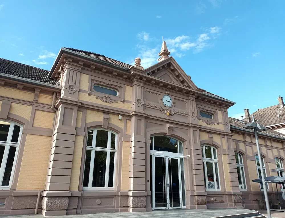 Bahnhof Baden-Baden: historisches Empfangsgebäude mit verzierter Sandsteinfassade, Uhr und großen Rundbogenfenstern