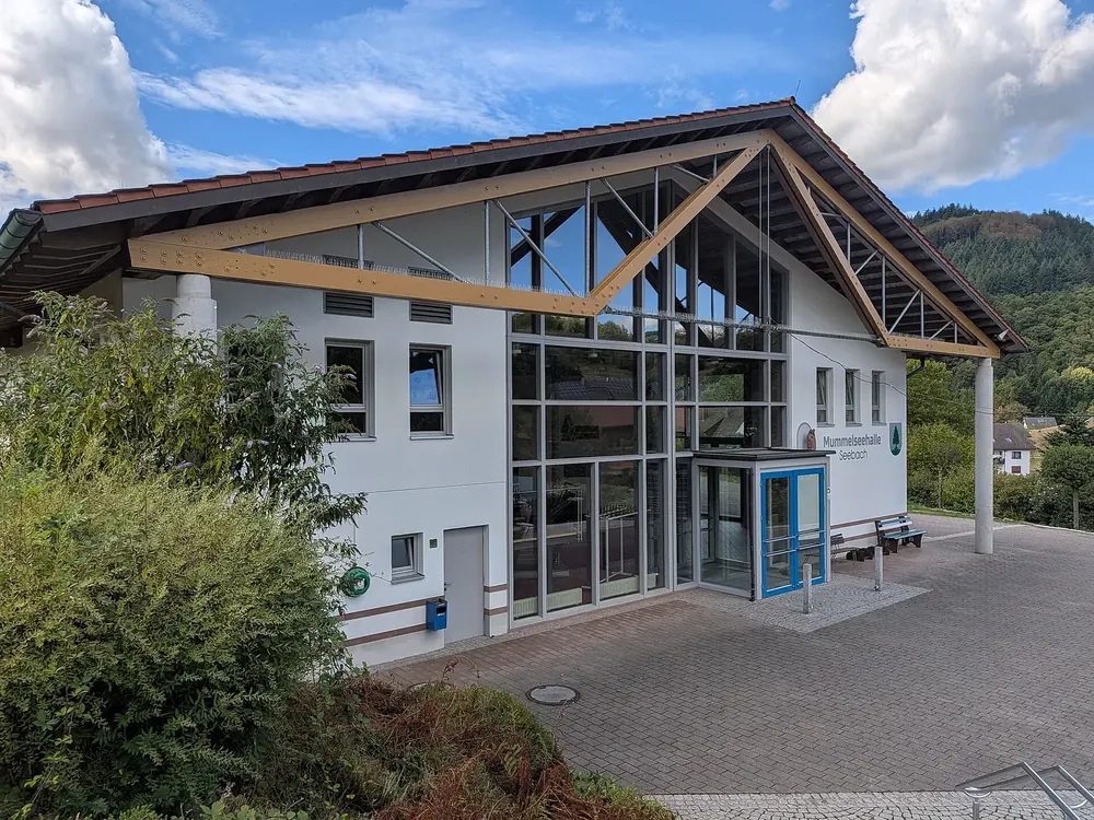 Mummelseehalle in Seebach: moderner Bau mit Glasfront und hölzernem Giebeldach vor bewaldeten Hängen