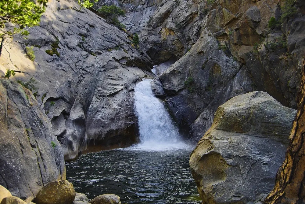 Roaring River Falls: Wasserfall stürzt durch eine enge Granitschlucht in ein dunkelgrünes Becken zwischen Felsblöcken
