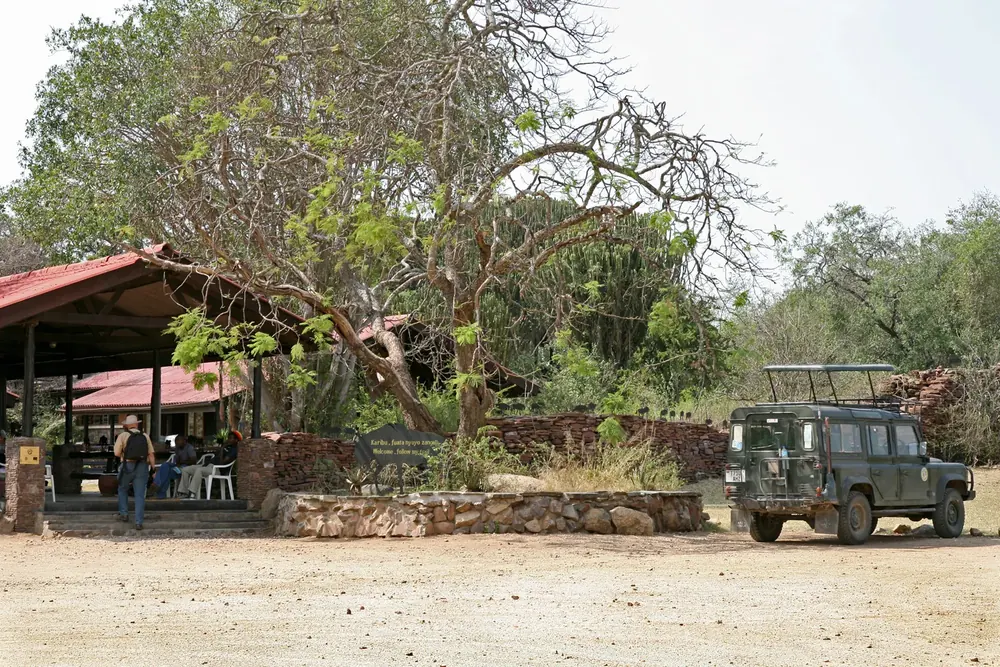 Serengeti Visitor Centre bei Seronera: offene Pavillons unter Bäumen, Steinmauern und ein Safari-Geländewagen