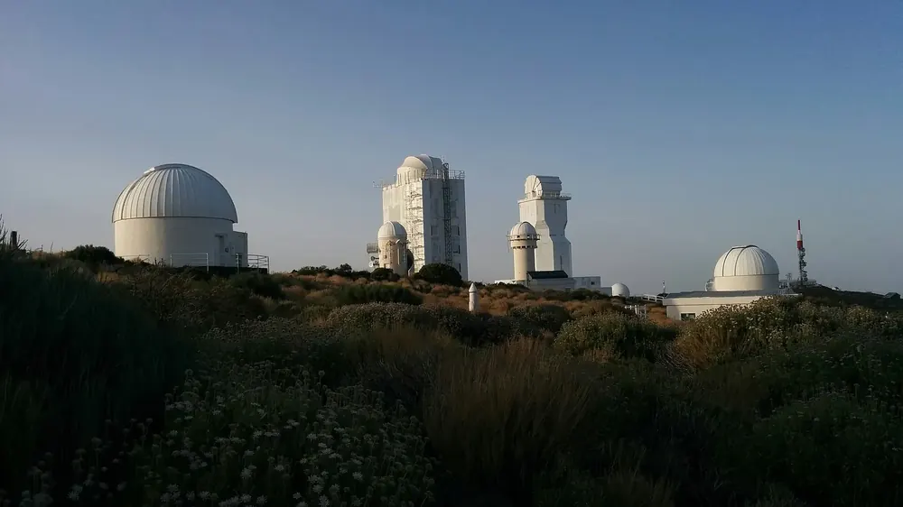 Observatorio del Teide: weiße Teleskopkuppeln und Sonnentürme über Ginsterbüschen im Abendlicht