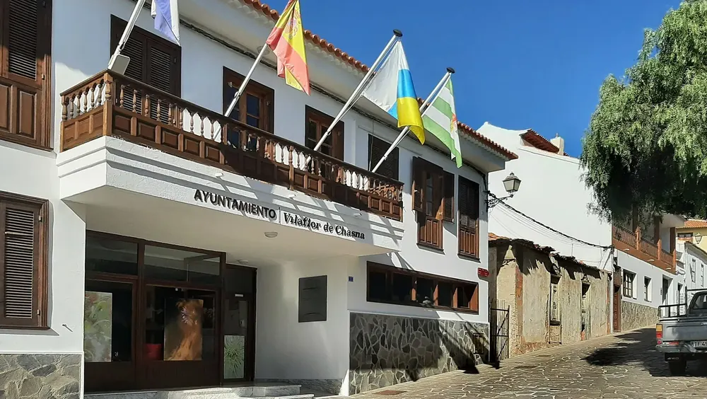 Weißes Gebäude mit Holzbalkonen und Fahnen an der Calle Francisco Ortuño in Vilaflor
