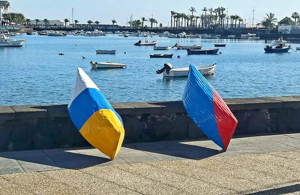 Zwei bunt bemalte Jolateros-Boote an der Hafenmauer in Arrecife, dahinter Fischerboote im blauen Wasser