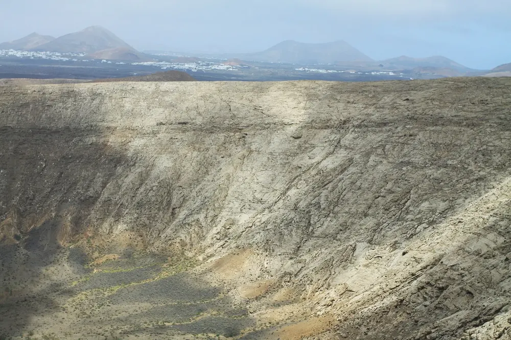 Caldera Blanca: steile, helle Innenwand des Tuffrings, dahinter weite Ebene und Vulkankegel Lanzarotes