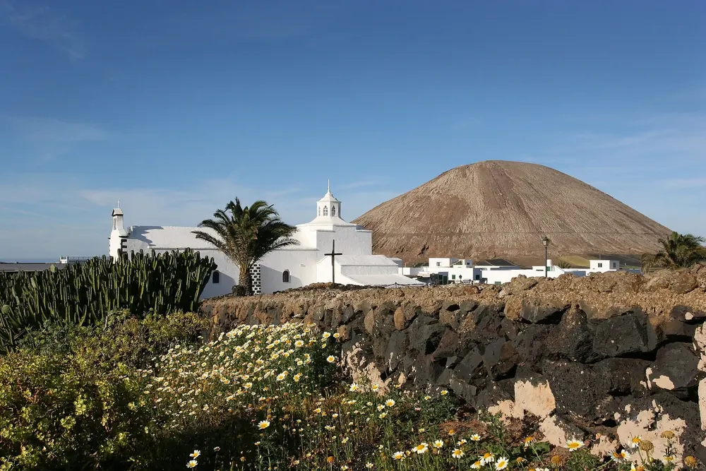 Mancha Blanca: weiße Kirche Nuestra Señora de los Dolores mit Palmen vor einem Vulkankegel