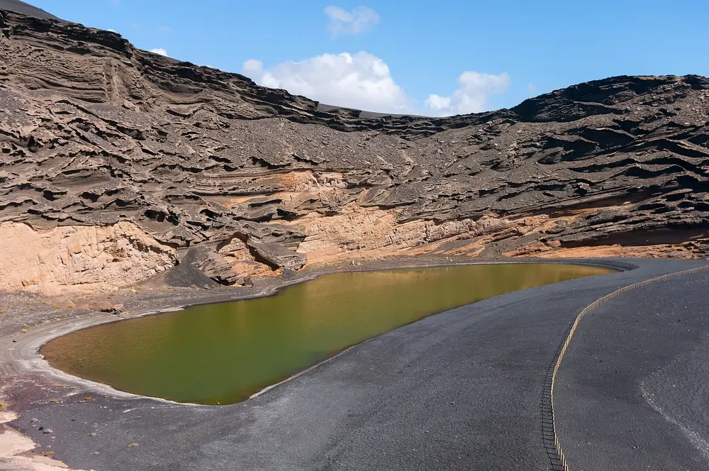 Charco de los Clicos: olivgrüne Lagune am schwarzen Strand unter den geschichteten Wänden des Kraters von El Golfo