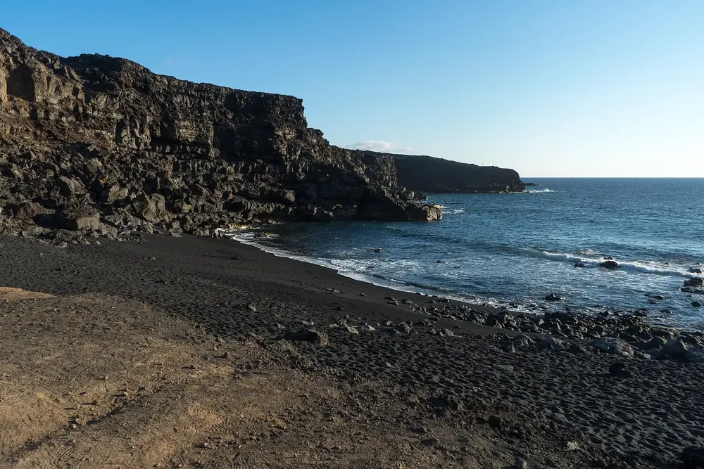 Playa del Paso: dunkler Kiesstrand unter schroffen Lavaklippen am tiefblauen Atlantik