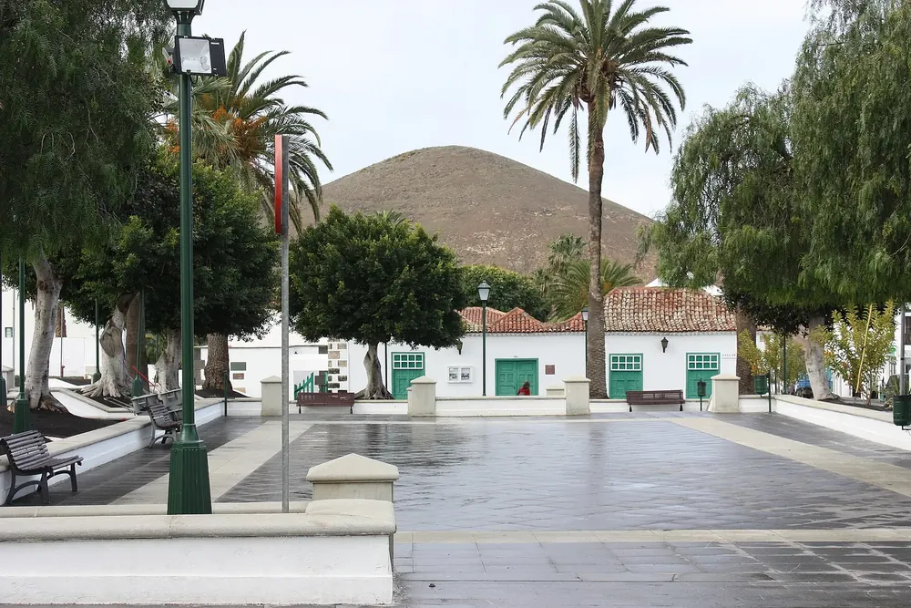 Plaza de los Remedios in Yaiza: gepflasterter Platz mit Palmen und weißen Häusern, dahinter ein Vulkankegel