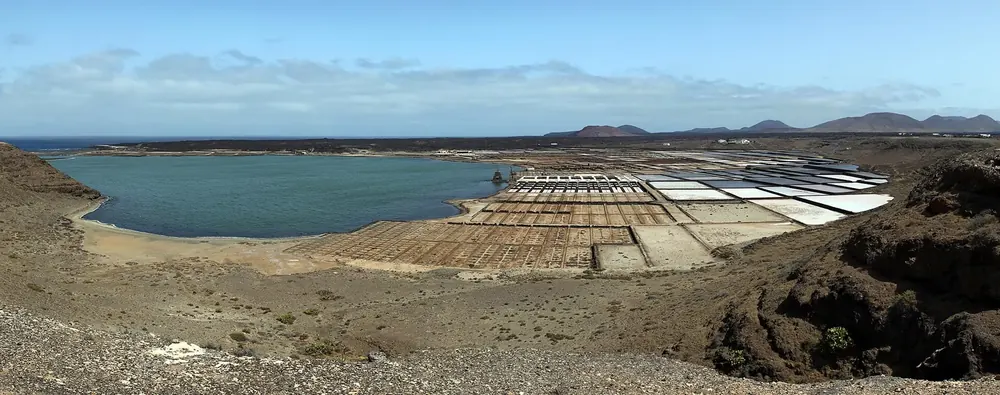 Salinas de Janubio: Lagune und schachbrettartige Salzbecken zwischen dunklen Vulkanhügeln an der Küste