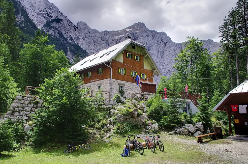Berghütte Aljažev dom im Vrata-Tal: Holzhaus mit steilem Dach vor der mächtigen Triglav-Nordwand, davor Fahrräder