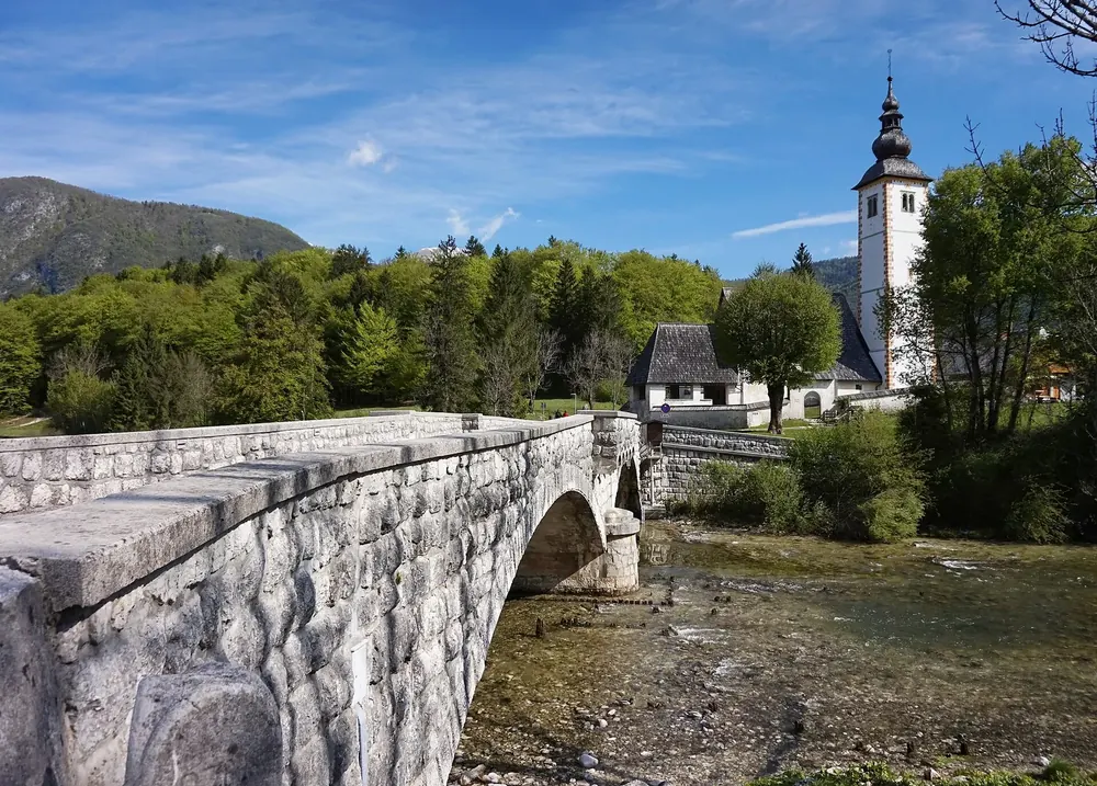 Ribčev Laz am Bohinjer See: steinerne Bogenbrücke über die Sava Bohinjka, dahinter die Kirche Johannes der Täufer
