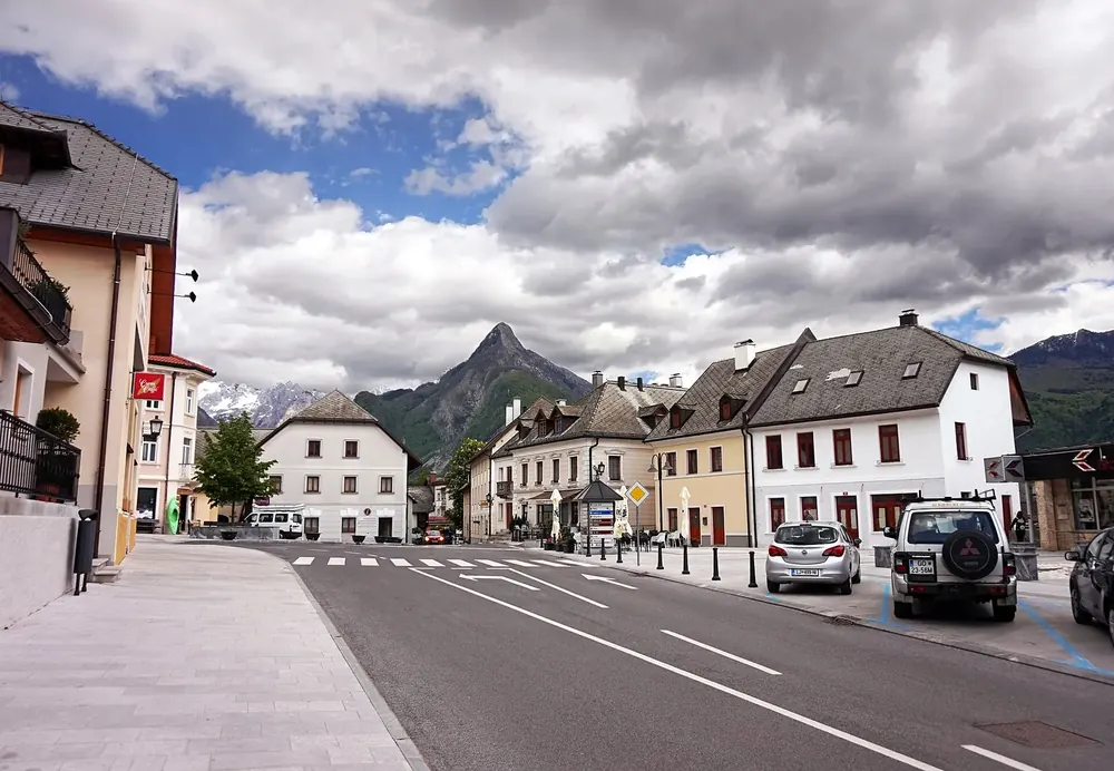 Trg golobarskih žrtev in Bovec: Hauptplatz mit Häusern und Kirche vor den Bergen der Julischen Alpen
