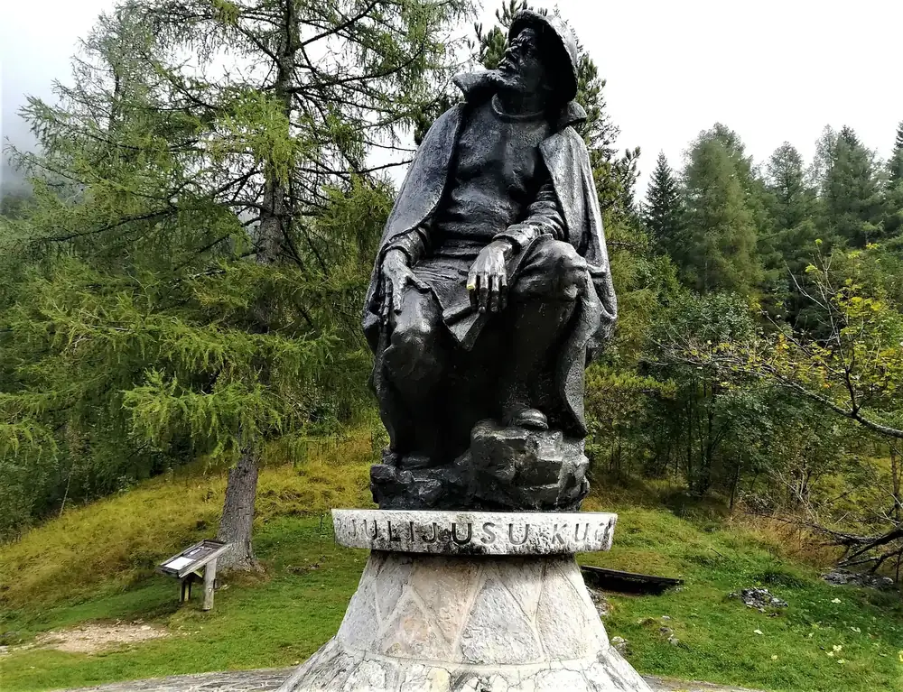 Kugy-Denkmal bei Trenta: Bronzestatue des Bergsteigers Julius Kugy auf einem Steinsockel vor Nadelbäumen