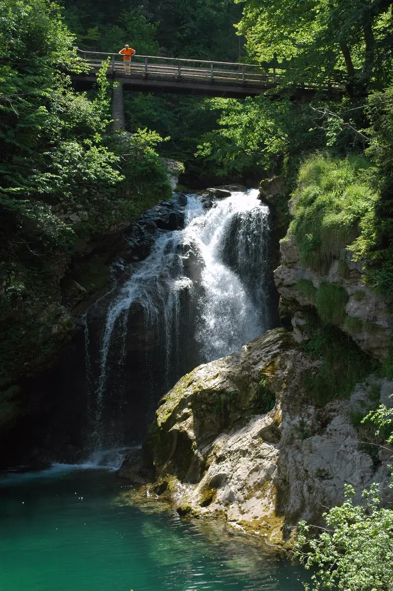 Wasserfall Šum am Ende der Vintgar-Klamm: Kaskade über Felsen in ein grünes Becken, oben eine Holzbrücke