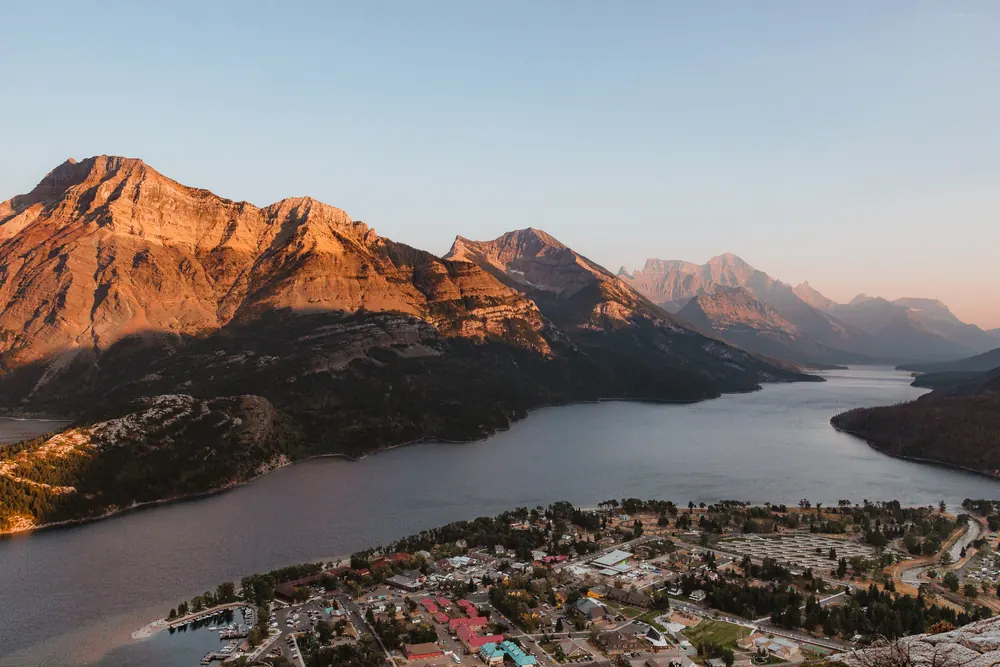 Blick vom Bear's Hump auf den Ort Waterton und den Upper Waterton Lake, dahinter Berge im warmen Streiflicht