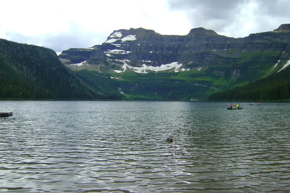 Blick über den Cameron Lake nach Süden auf Felswände und Schneefelder, auf dem See kleine Kanus