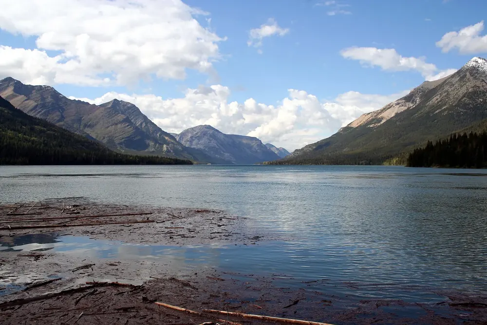 Upper Waterton Lake: weiter Bergsee zwischen steilen, bewaldeten Hängen, vorn flache Felsplatten am Ufer