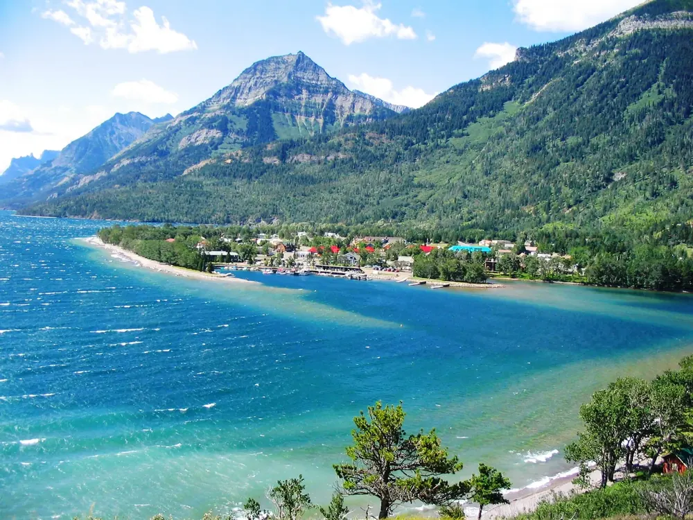 Blick vom Prince of Wales Hotel auf Waterton Park am türkisblauen Upper Waterton Lake vor bewaldeten Bergen