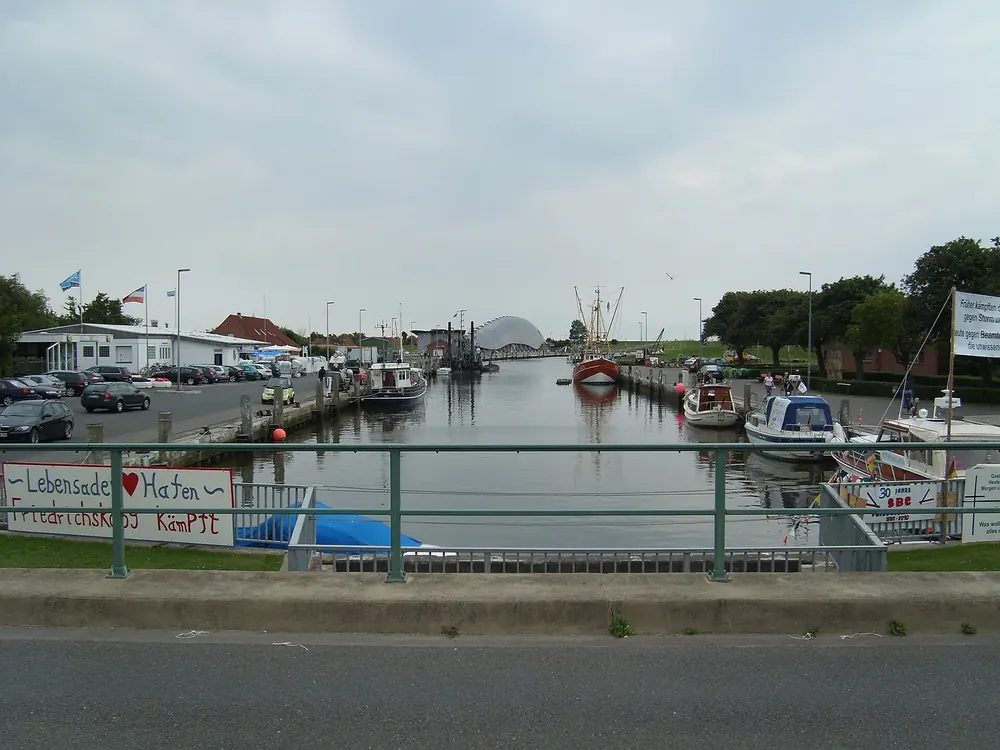 Hafen von Friedrichskoog: Kutter und Boote im schmalen Hafenbecken, am Ufer Gebäude und Parkplätze