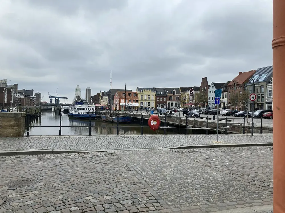 Binnenhafen von Husum: Kopfsteinpflaster am Kai, Schiffe im Hafenbecken und Giebelhäuser unter Wolken